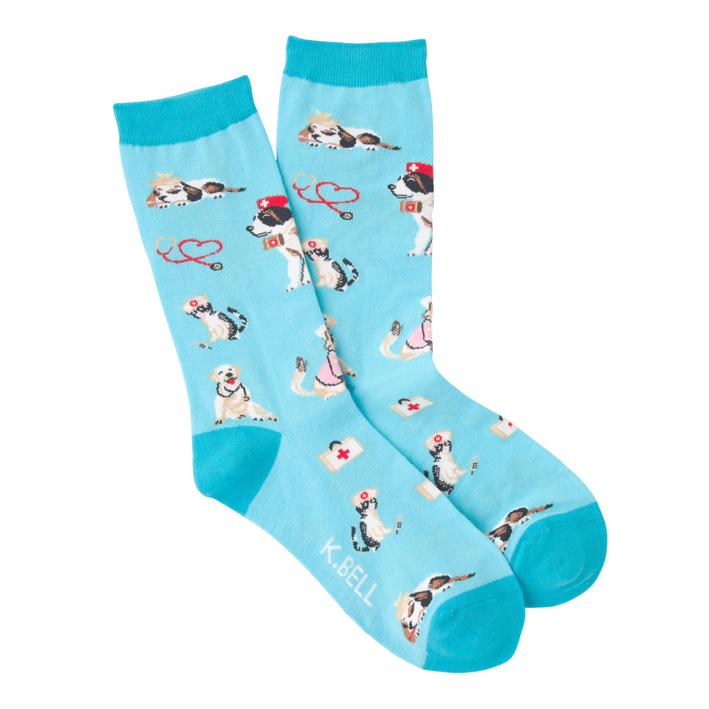 K Bell Womens Veterinarian Sock starts on a Turquoise Blue background with Teal Cuffs, Heels and Toes. All around the Sock are Dogs and Cats playing Veterinarians. At least one is playing a patient! All over you see Red or Black Stethoscopes being used by Vets in Medical Hats.